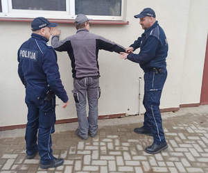 policjanci z zatrzymanym, jeden z nich nakłada mężczyźnie kajdanki