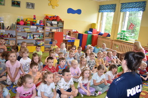 spotkanie z dziećmi w PP nr 2 w Bartoszycach, plecy siedzącej policjantki w tle grupa siedzących na dywanie przedszkolaków