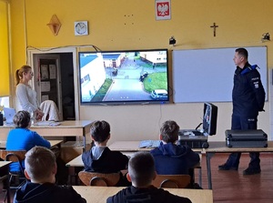 policjant przy tablicy multimedialnej  w trakcie spotkania z dziećmi